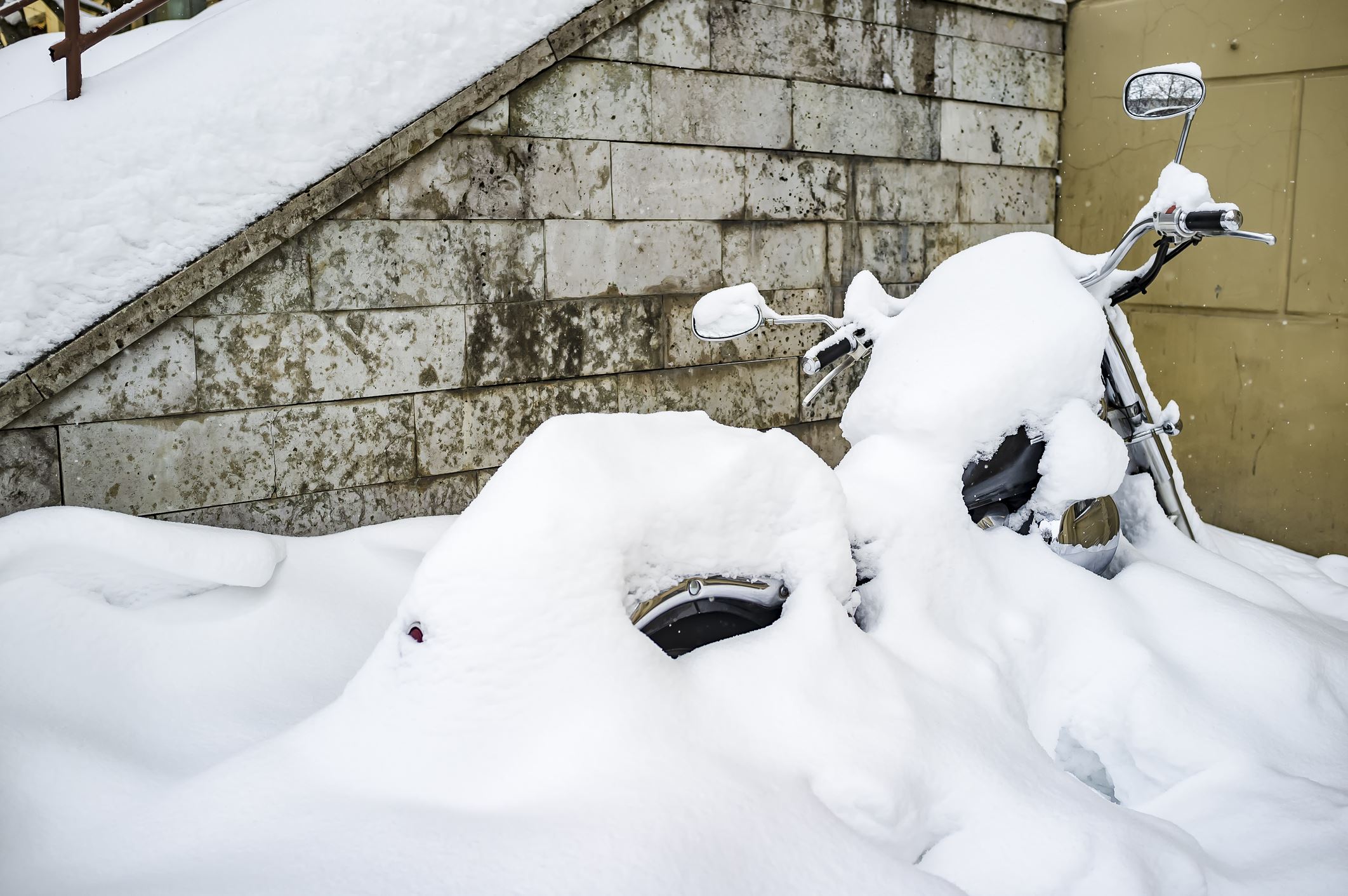 Winter in Russia. Motorcycle parked near the wall of the house is almost completely covered with snow and waiting for spring, and the beginning of the season for long journeys. (Winter in Russia. Motorcycle parked near the wall of the house is almost
