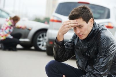 Man sitting outside car, holding head, after accident