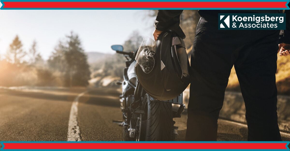 motorcyclist standing behind motorcycle, holding helmet in hand