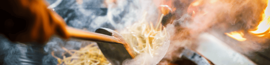 Chef in restaurant kitchen at stove with high burning flames